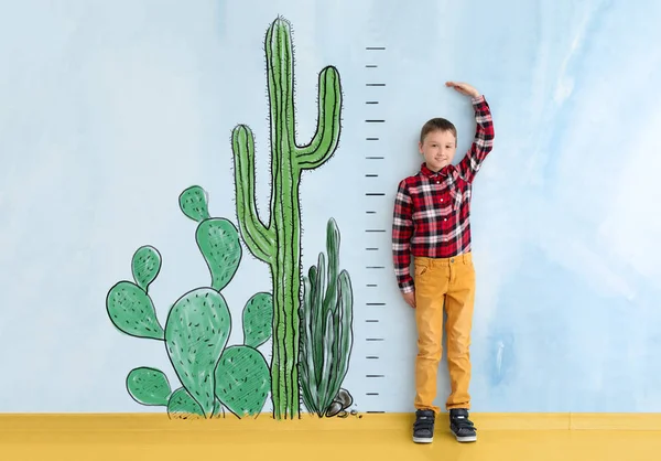 Lindo niño midiendo altura cerca de la pared de color con cactus dibujados — Foto de Stock