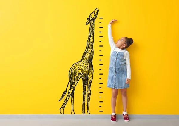 Surprised African-American girl measuring height near color wall with drawn giraffe — Stock Photo, Image