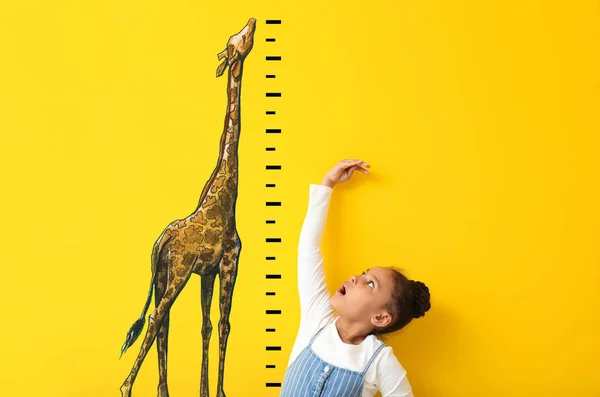 Chica afroamericana sorprendida midiendo altura cerca de la pared de color con jirafa dibujada — Foto de Stock