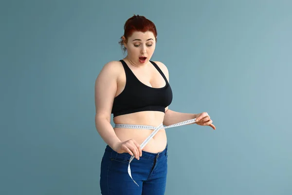 Mujer sobrepeso conmocionada con cinta métrica en el fondo de color. Concepto de pérdida de peso — Foto de Stock