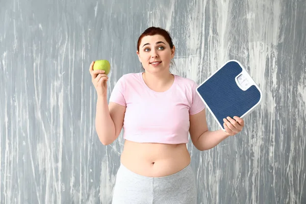 Overweight woman with scales and apple on grey background. Weight loss concept — Stock Photo, Image