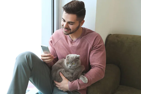 Young man with cute funny cat and mobile phone at home — Stock Photo, Image