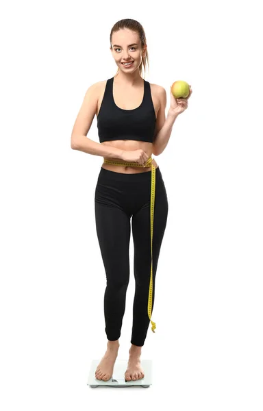 Mulher jovem com maçã e fita métrica em pé em escalas contra fundo branco. Conceito de perda de peso — Fotografia de Stock