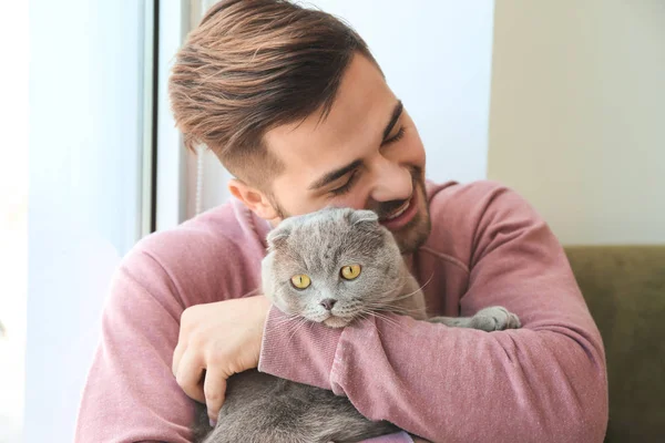 Young man with cute funny cat near window — Stock Photo, Image