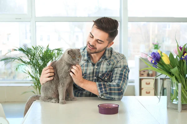 Young man feeding cute funny cat at home — Stock Photo, Image