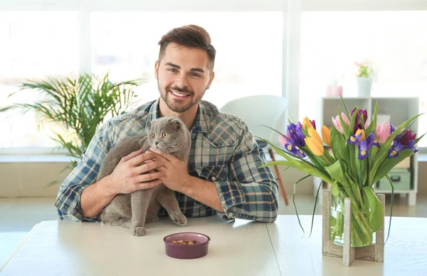 Young man feeding cute funny cat at home — Stock Photo, Image