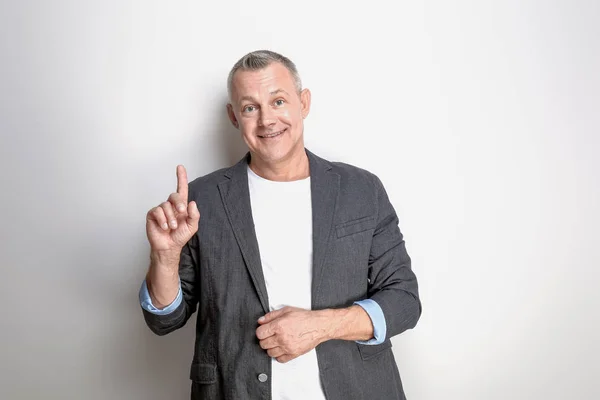 Portrait of handsome middle-aged man with raised index finger on light background — Stock Photo, Image
