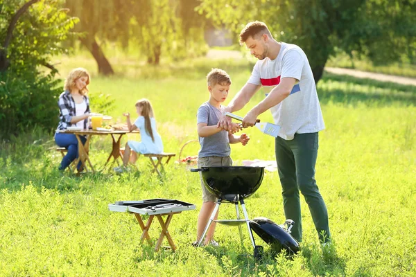 Padre con figlio cucinare cibo gustoso sulla griglia all'aperto — Foto Stock