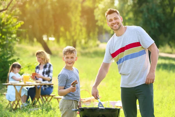 Padre con figlio cucinare cibo gustoso sulla griglia all'aperto — Foto Stock