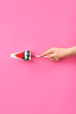Renk arka plan üzerinde lezzetli Blueberry cheesecake parçası ile kadın el