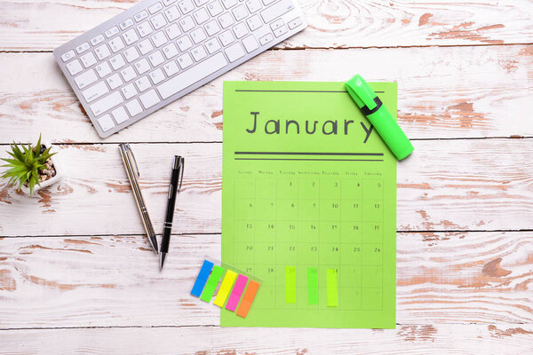 Бумажный календарь, клавиатура и канцелярские принадлежности на светлом деревянном фоне
