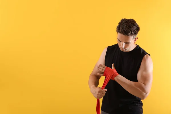 Joven deportivo aplicando muñequeras sobre fondo de color — Foto de Stock