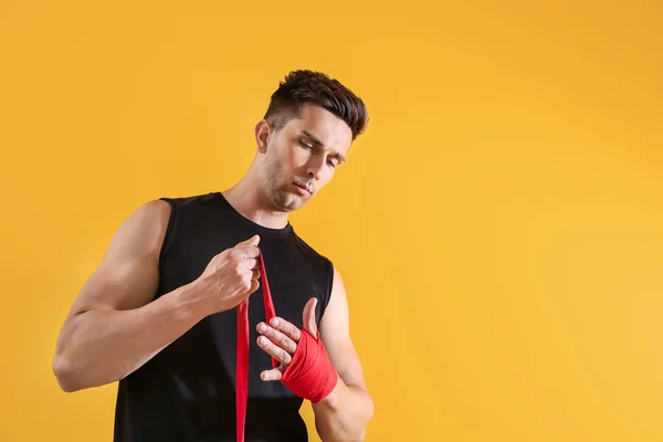 Joven deportivo aplicando muñequeras sobre fondo de color — Foto de Stock