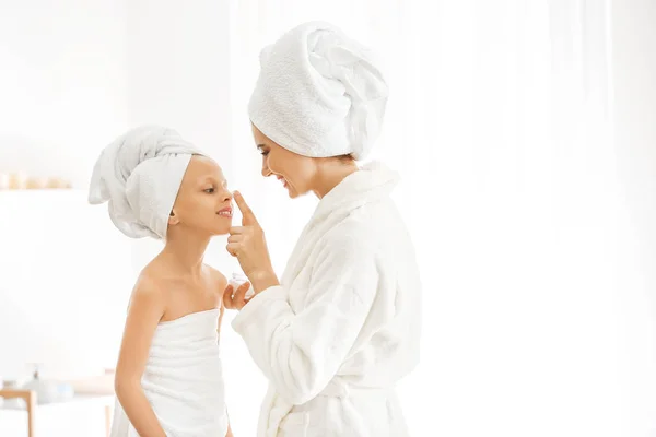 Мати наносить крем на обличчя своєї маленької дочки у ванній — стокове фото