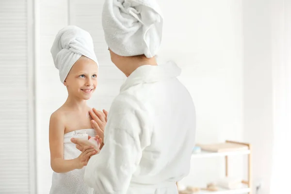 Moeder aanbrengt crème op de huid van haar kleine dochter in de badkamer — Stockfoto