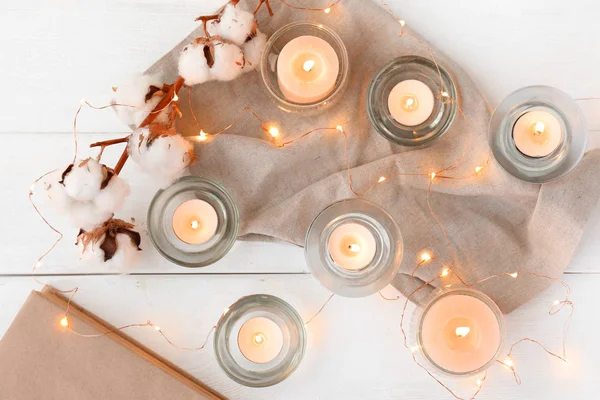 Lindas velas acesas com flores de algodão e guirlanda em fundo de madeira branca — Fotografia de Stock