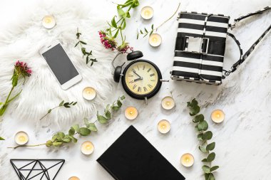 Çalar saat, cep telefonu, çanta ve ışık arka planda kitap ile güzel yanan mumlar