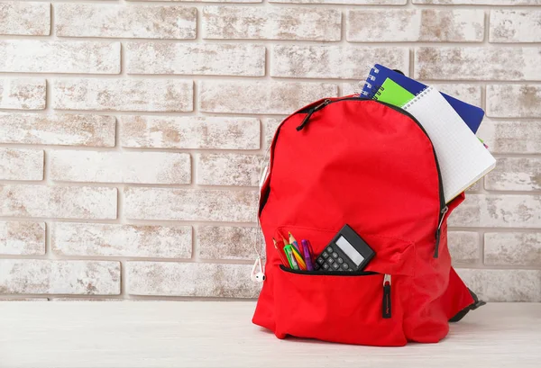 Mochila escolar con papelería en la mesa contra la pared de ladrillo — Foto de Stock