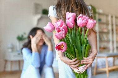 Evde arka arkasında anne için çiçek buket tutan küçük kız