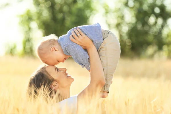 Schöne Frau spielt mit ihrem kleinen Sohn im Weizenfeld an einem Sommertag — Stockfoto