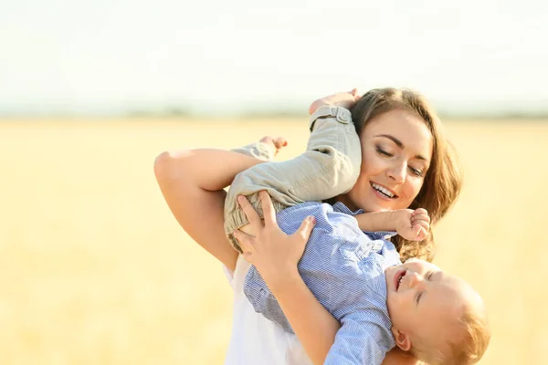 Schöne Frau spielt mit ihrem kleinen Sohn im Weizenfeld an einem Sommertag — Stockfoto