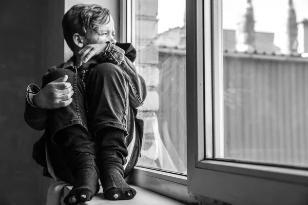 Petit garçon sans abri assis sur le rebord de la fenêtre à l'intérieur — Photo