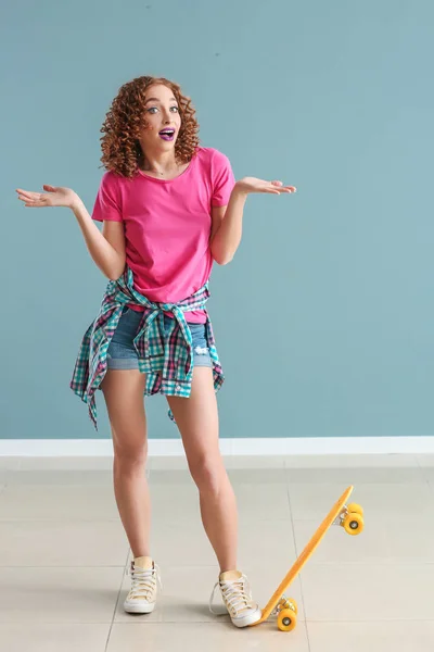 Jeune femme émotionnelle avec planche à roulettes près du mur gris — Photo