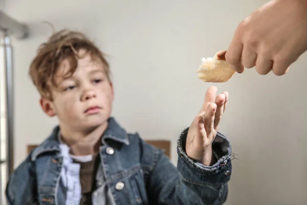 Woman giving food to homeless little boy indoors — Stock Photo, Image