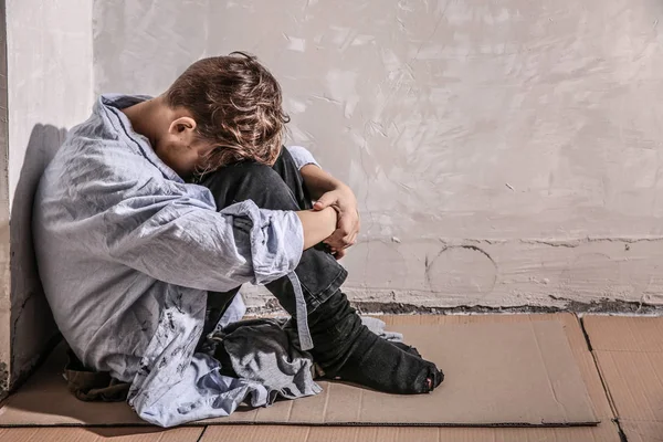 Petit garçon sans abri assis sur le sol près du mur — Photo