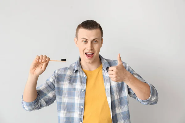 Happy man with toothbrush showing thumb-up gesture on light background — Stock Photo, Image