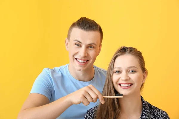 Hombre feliz ayudando a su novia a limpiar los dientes contra el fondo de color — Foto de Stock