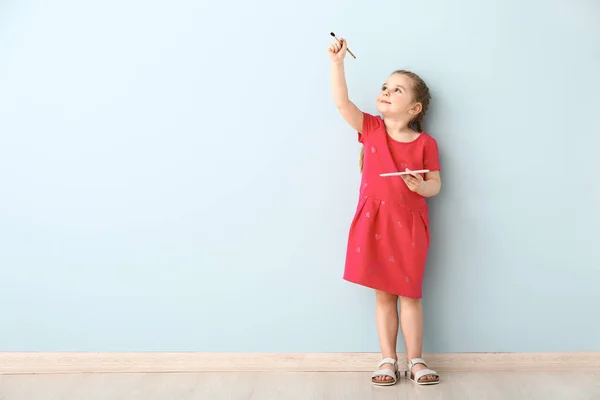 Маленькая девочка с кистью и палитрой возле светлой стены — стоковое фото