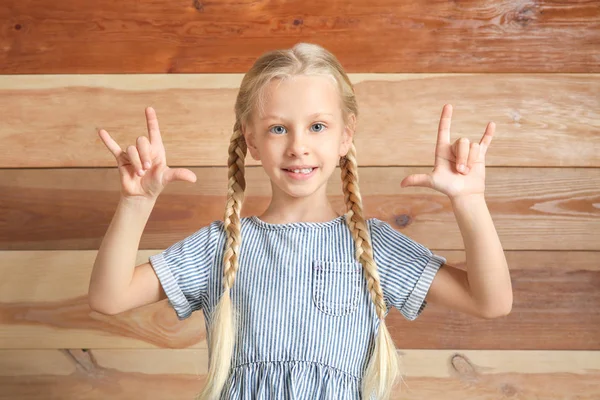 Little deaf mute girl using sign language on wooden background