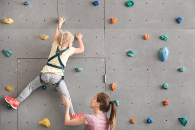 Eğitmen küçük kız spor salonunda duvara tırmanmaya yardım