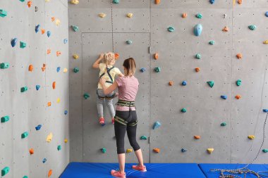 Eğitmen küçük kız spor salonunda duvara tırmanmaya yardım