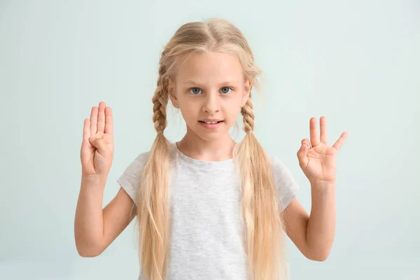 Kleines taubstummes Mädchen mit Gebärdensprache auf hellem Hintergrund — Stockfoto