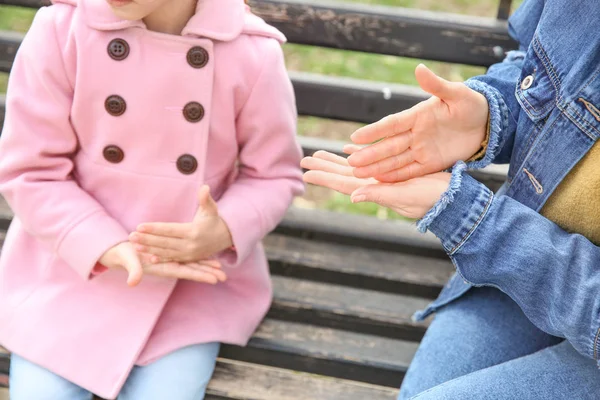 Mother teaching her deaf mute daughter to use sign language outdoors