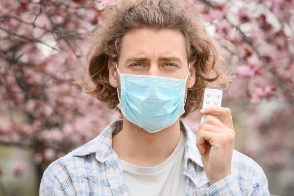 Young man in protective mask and with pills near blooming tree — Stock Photo, Image