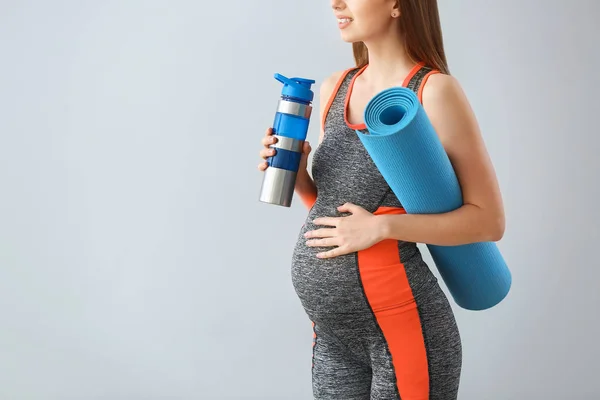 Beautiful pregnant woman with yoga mat and bottle of water on grey background — Stock Photo, Image