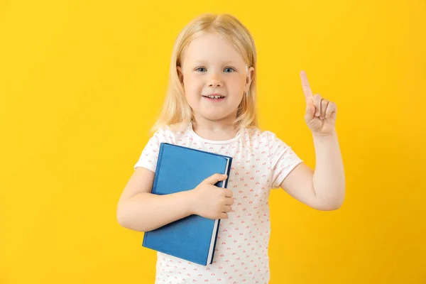 Portrait of adorable little girl with book and raised index finger on color background