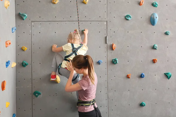 Instrutor ajudando a menina a subir parede no ginásio — Fotografia de Stock