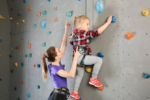 Instruktor pomaga małej dziewczynie wspiąć się na ścianie w siłowni — Zdjęcie stockowe