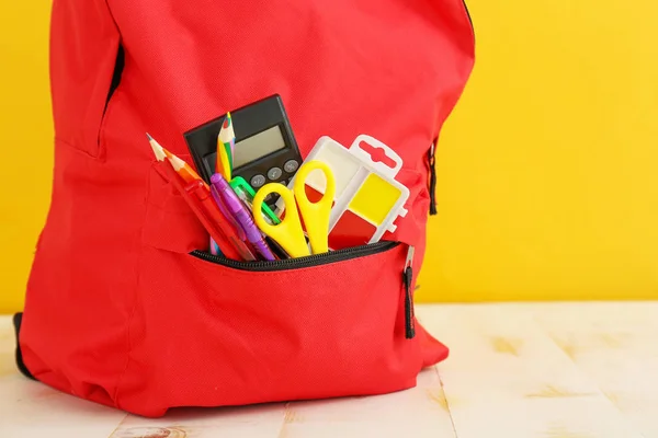 Школьный рюкзак с канцелярскими принадлежностями на столе на фоне цвета — стоковое фото