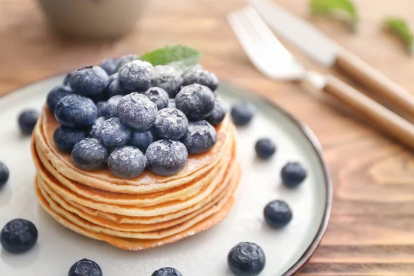 Teller mit leckeren Pfannkuchen und Blaubeeren auf Holztisch — Stockfoto