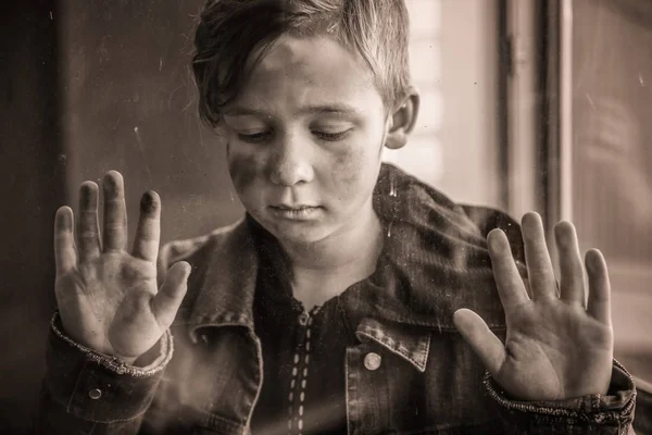 Бездомный мальчик возле окна, вид через стекло — стоковое фото