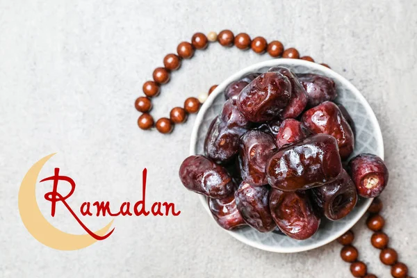 Plate with tasty dates, tasbih and word RAMADAN on light background — Stock Photo, Image