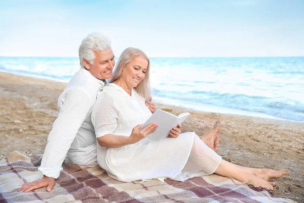 Happy mature couple reading book at sea resort — Stock Photo, Image
