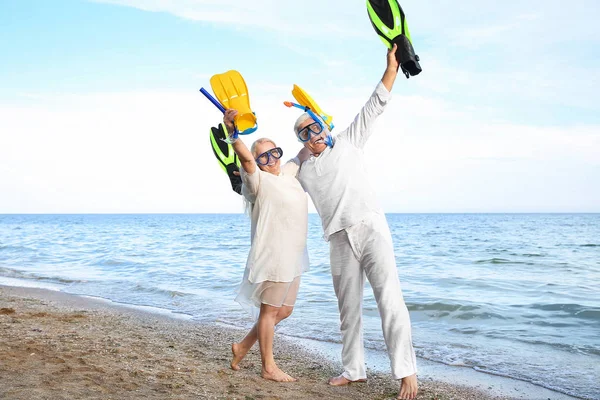 Happy mature couple with snorkeling masks and paddles having fun at sea resort — Stock Photo, Image