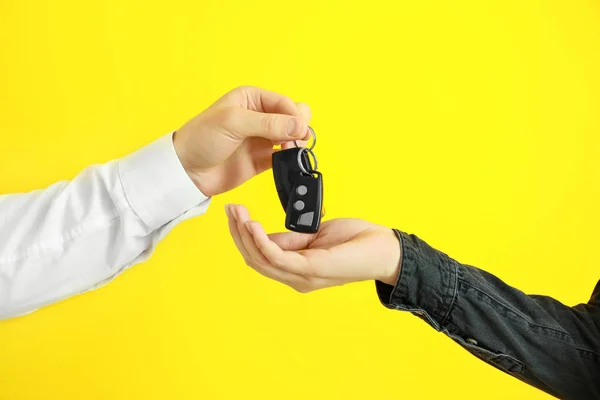 Verkäufer gibt Autoschlüssel an Frau auf farbigem Hintergrund — Stockfoto