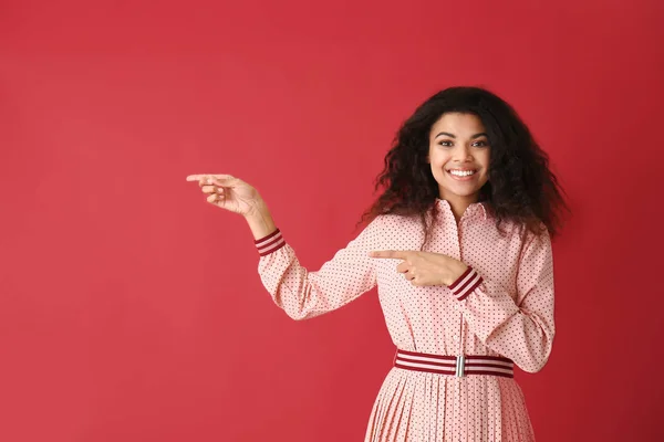 Portrait of happy African-American woman pointing at something on color background — Stock Photo, Image